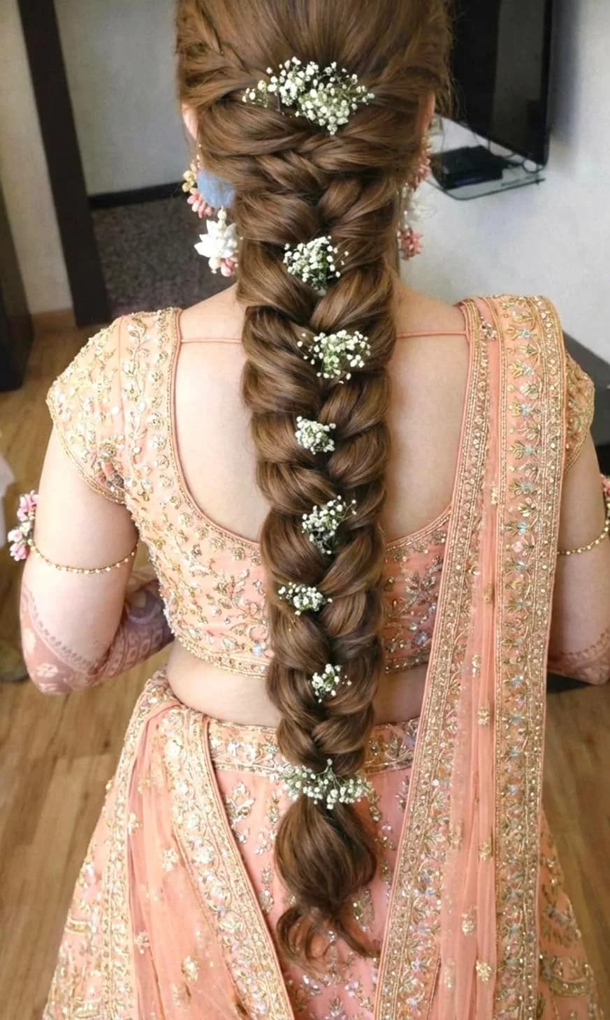 Long textured bridal braid trailed with baby’s breath, worn with a peach lehenga