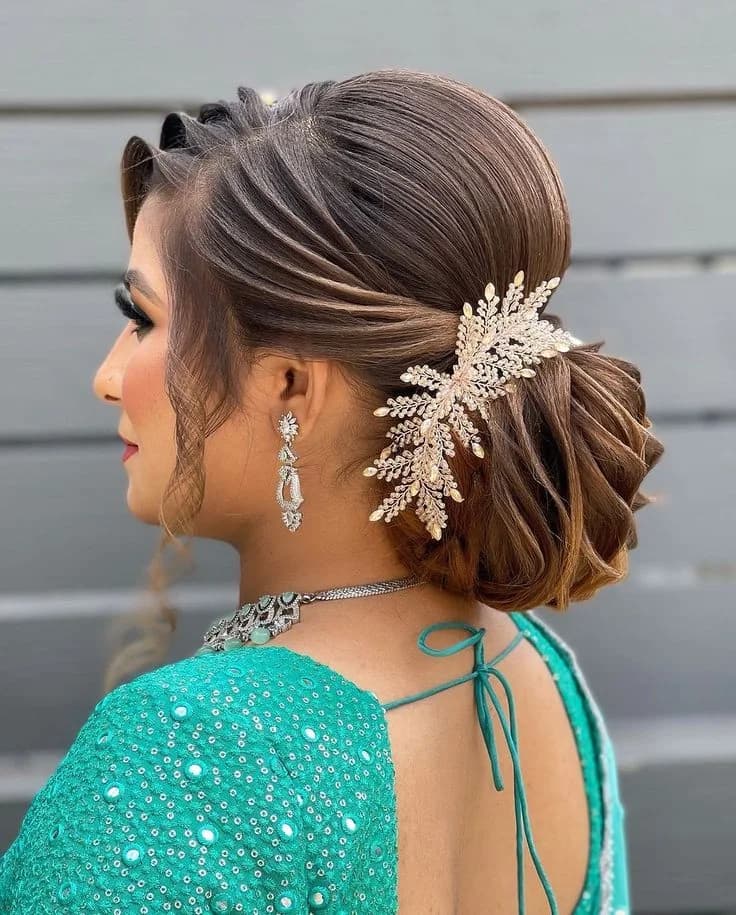 Side-swept low bun finished with a crystal leaf hairpiece, worn with a teal outfit