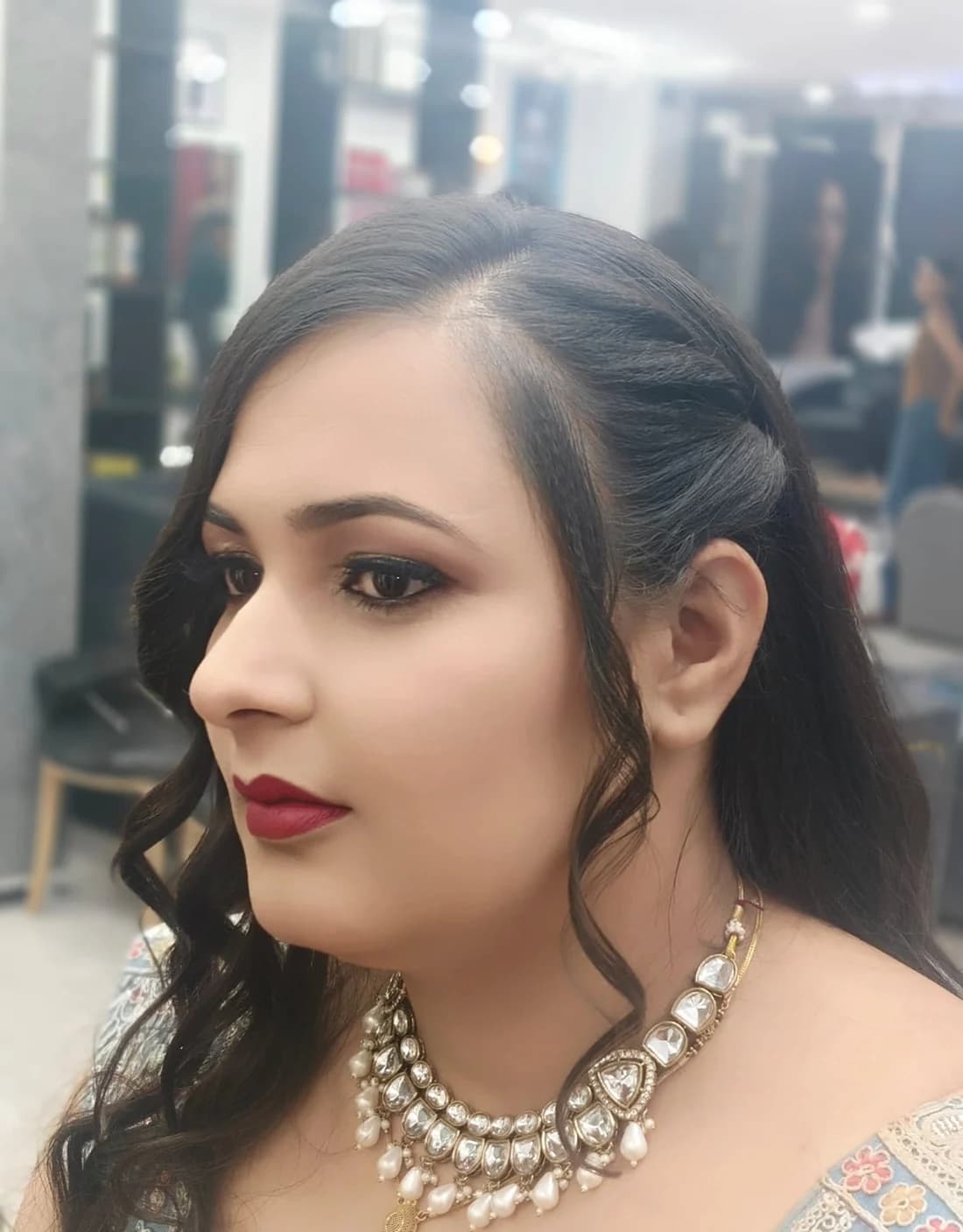 Side profile of an occasion look with a deep berry lip, smoky liner and soft face-framing waves