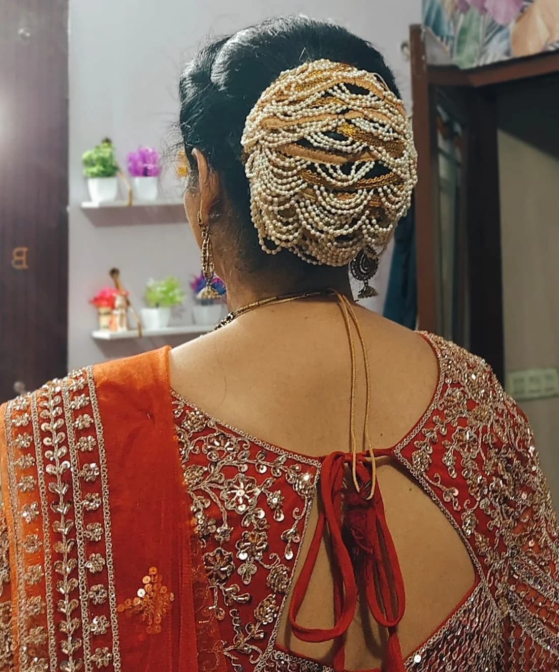Bridal juda dressed with layered pearl and gold strings, worn with an orange lehenga